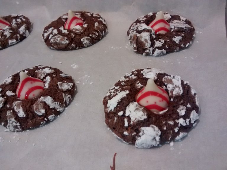 Chocolate crinkle cookies with red and white striped kisses on parchment paper