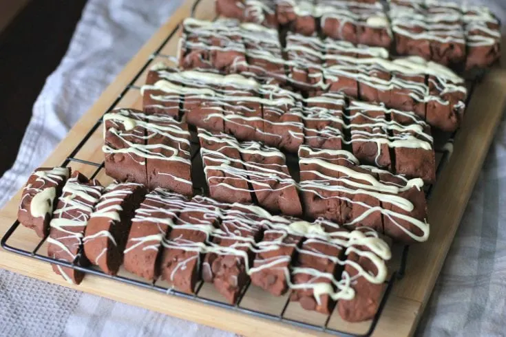 Brownie biscotti with white chocolate drizzle on a cooling rack.