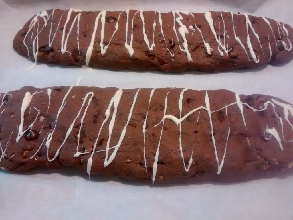 Chocolate Biscotti Logs cooling on baking sheet with white chocolate drizzle 