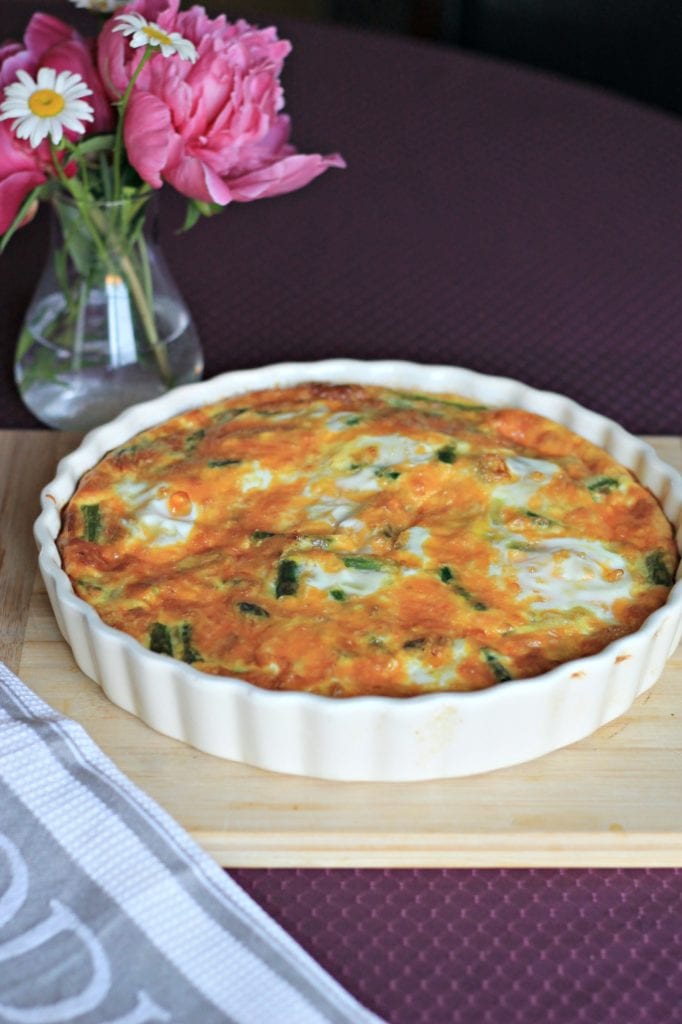 Finished quiche in cream quiche dish on wooden cutting board