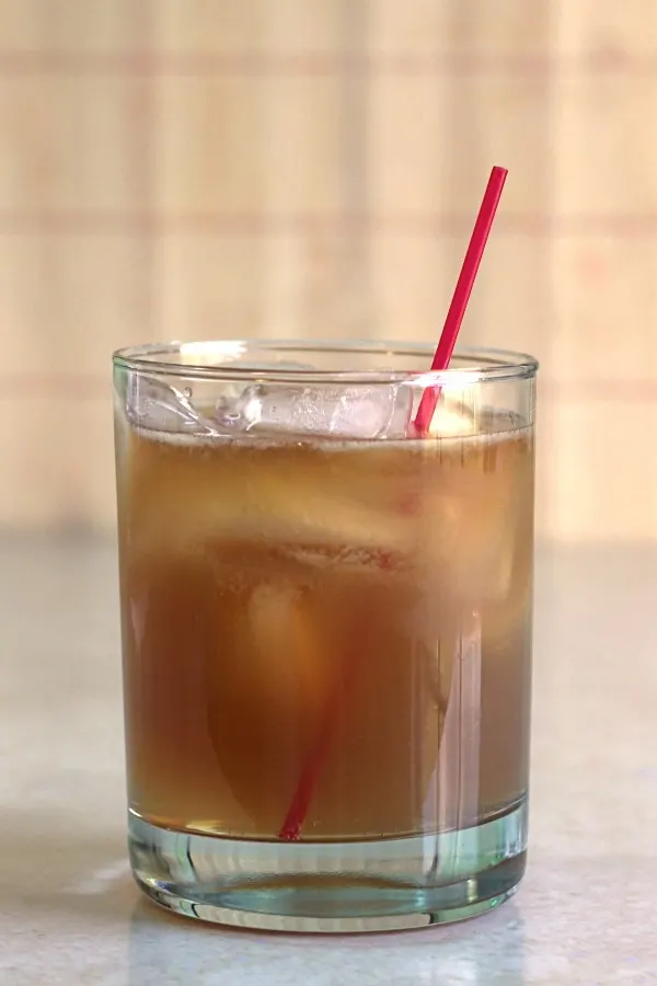 Bourbon cocktail in clear tumbler with red straw