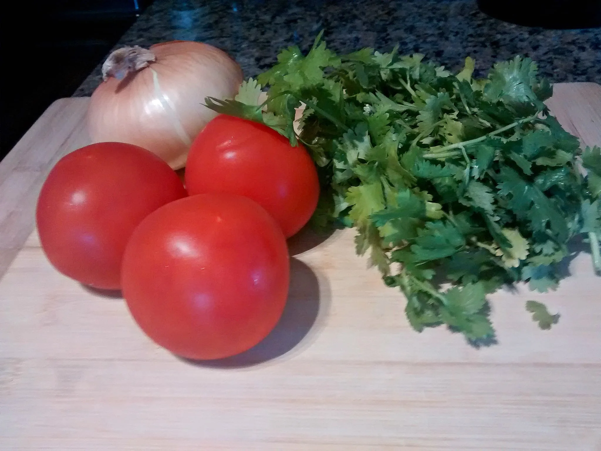 Fresh tomatoes, onion and cilantro on wood cutting board for salsa 
