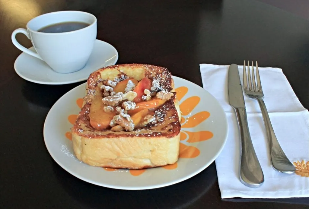 Stuffed French Toast with fresh peaches on a floral plate with cup of coffee