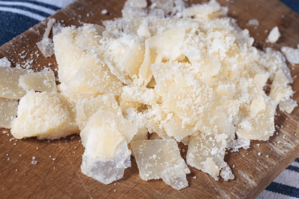 Parmesan flakes on wooden cutting board.