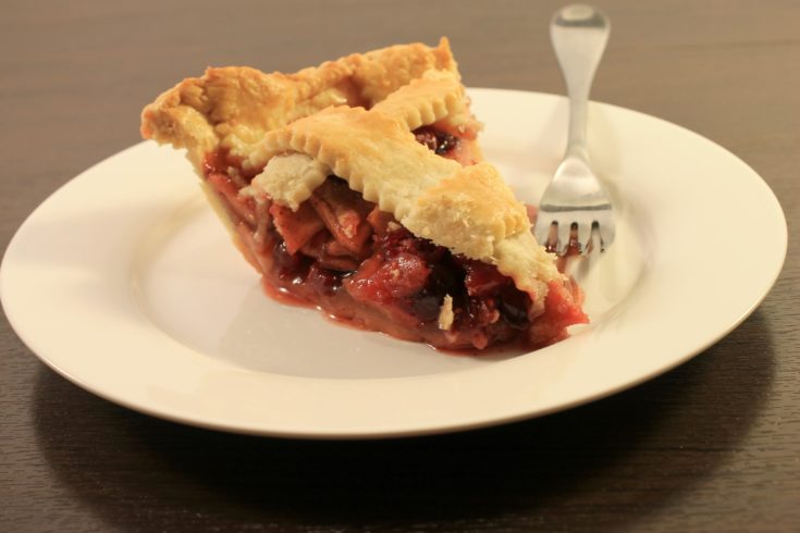Slice of cranberry apple pie on white ceramic dish with fork