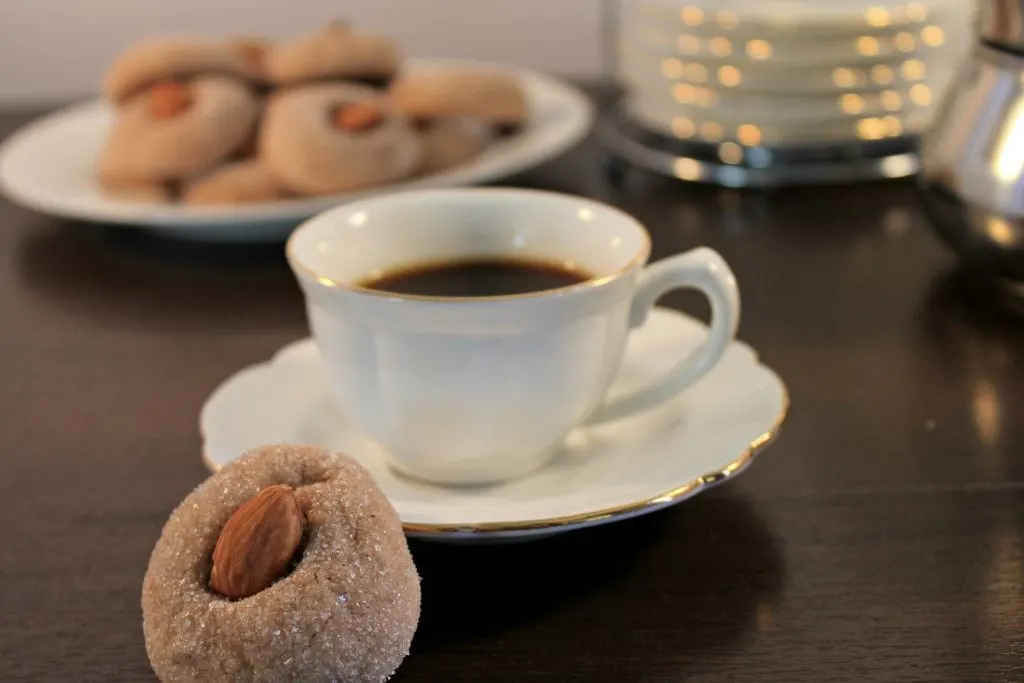 Amaretti cookie leaning on espresso cup and saucer with plate of cookies in the back 