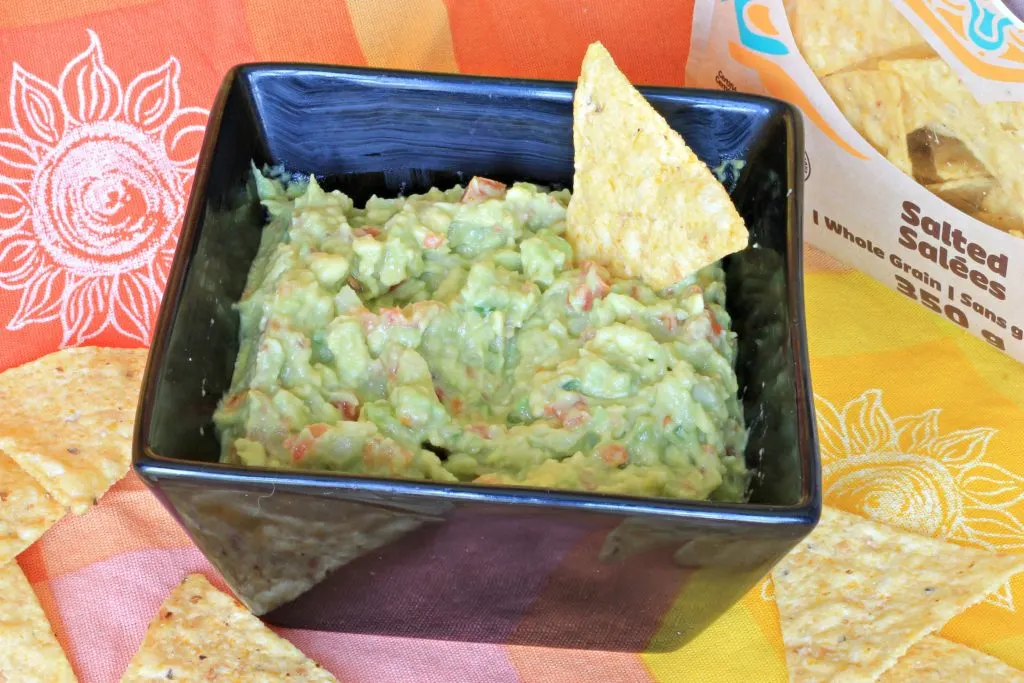 Black square bowl full of fresh guacamole with tortilla corn chip