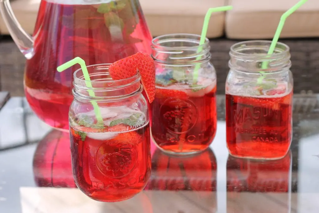 Strawberry Mint Cocktail Drink in clear glass pitcher on patio table with mason jar glasses