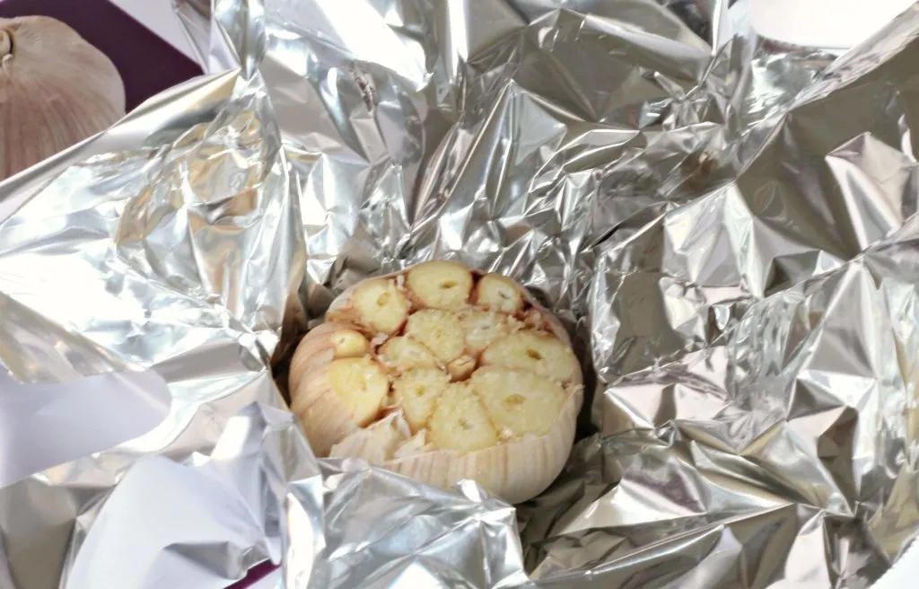 whole garlic bulb with top sliced off sitting in foil.