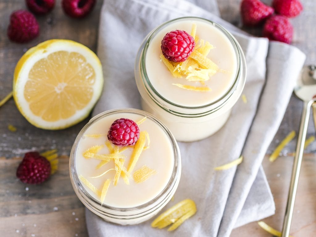 Glass jars with yogurt topped with fresh raspberries and lemon zest
