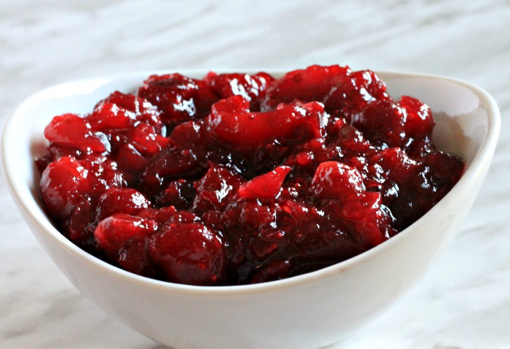 Cranberry sauce in white ceramic bowl on marble counter.