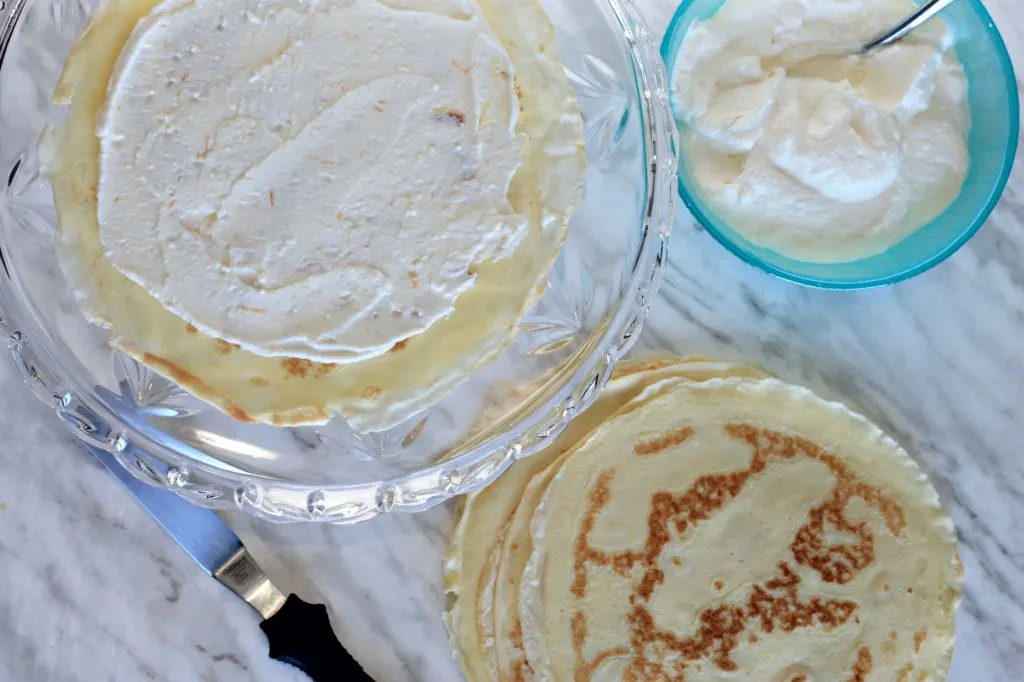 cake stand with frosted crepe and pile of crepes next to it