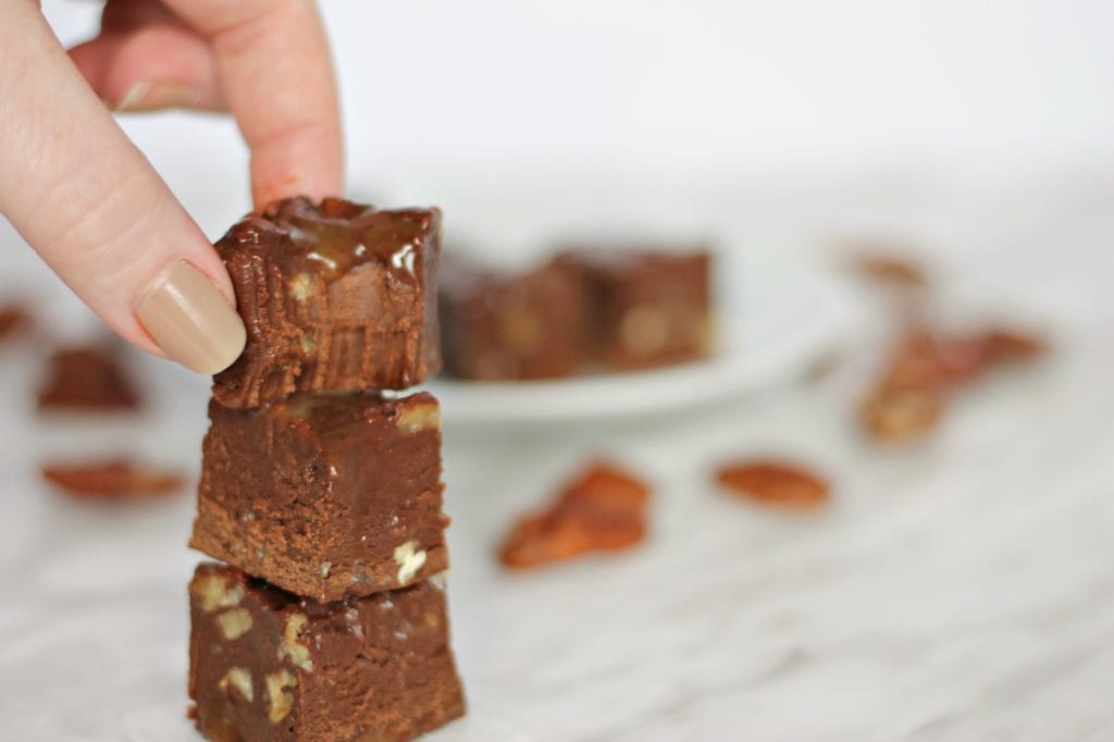 3 sqaures of chocolate fudge stacked with pecans scattered behind