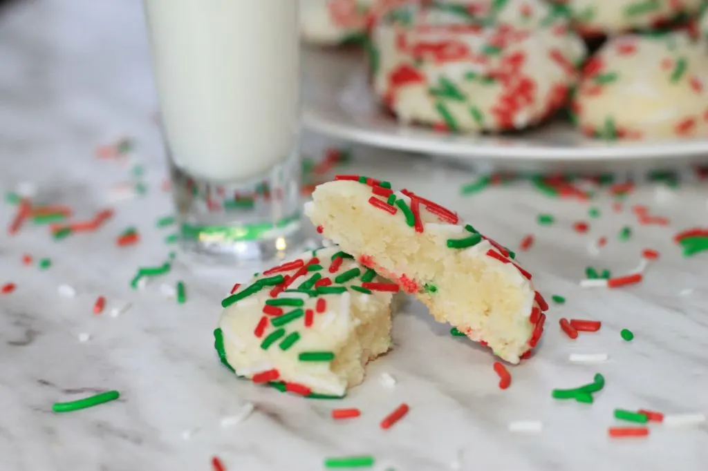 Sprinkle Cookie on marble countertop with festive sprinkles scattered around and a glass with milk.