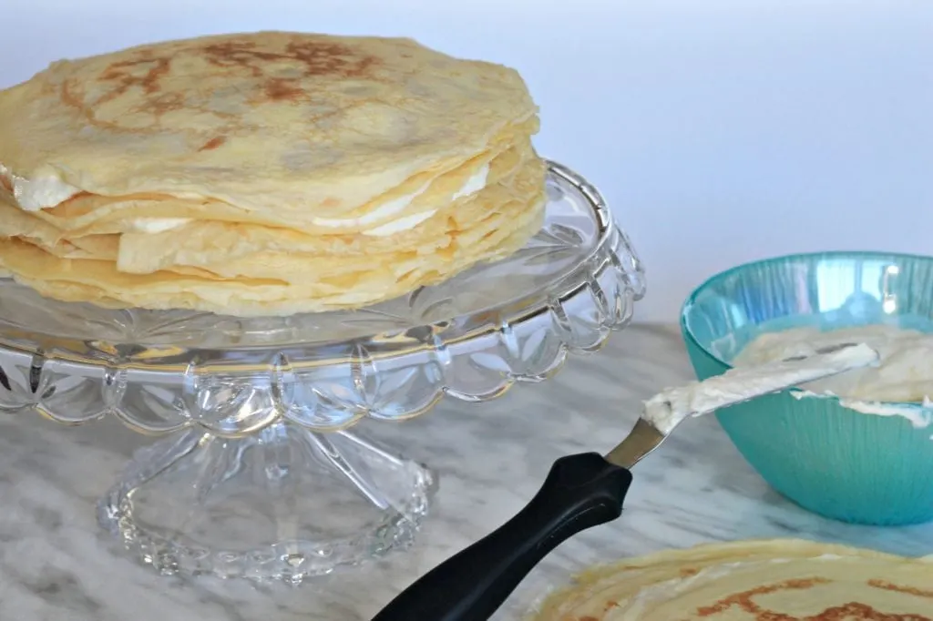 Multiple crepes stacked with cream filling on glass cake stand
