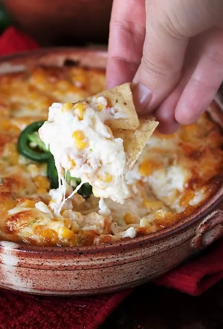 Brown dish full of hot corn dip being scooped out with corn chip