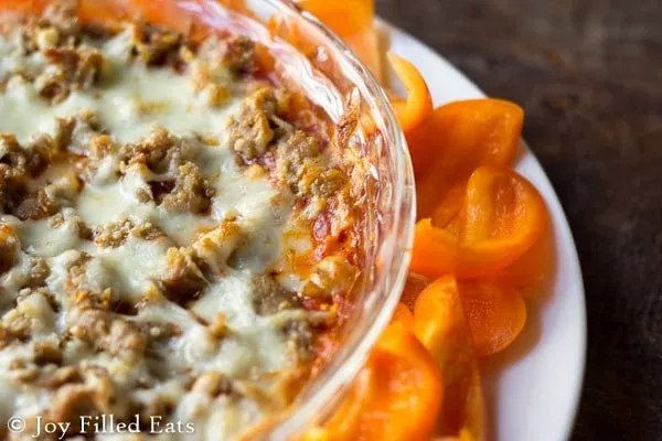 Hot Pizza Dip in glass bowl on white plate with fresh vegetables