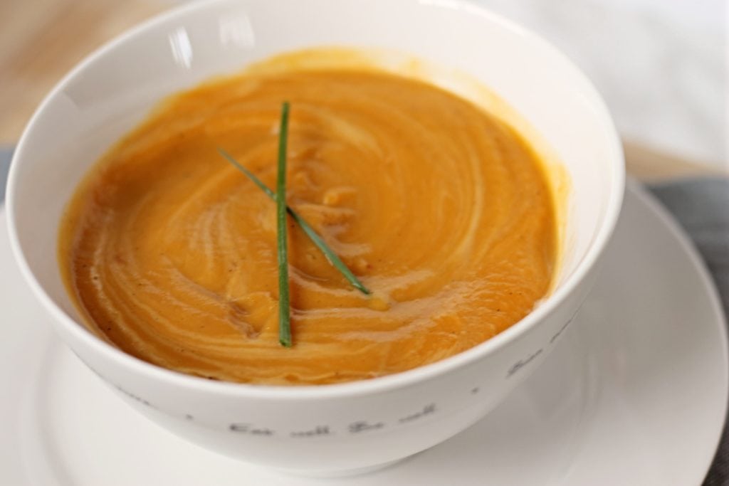 White ceramic bowl with Sweet Potato Soup topped with fresh chives