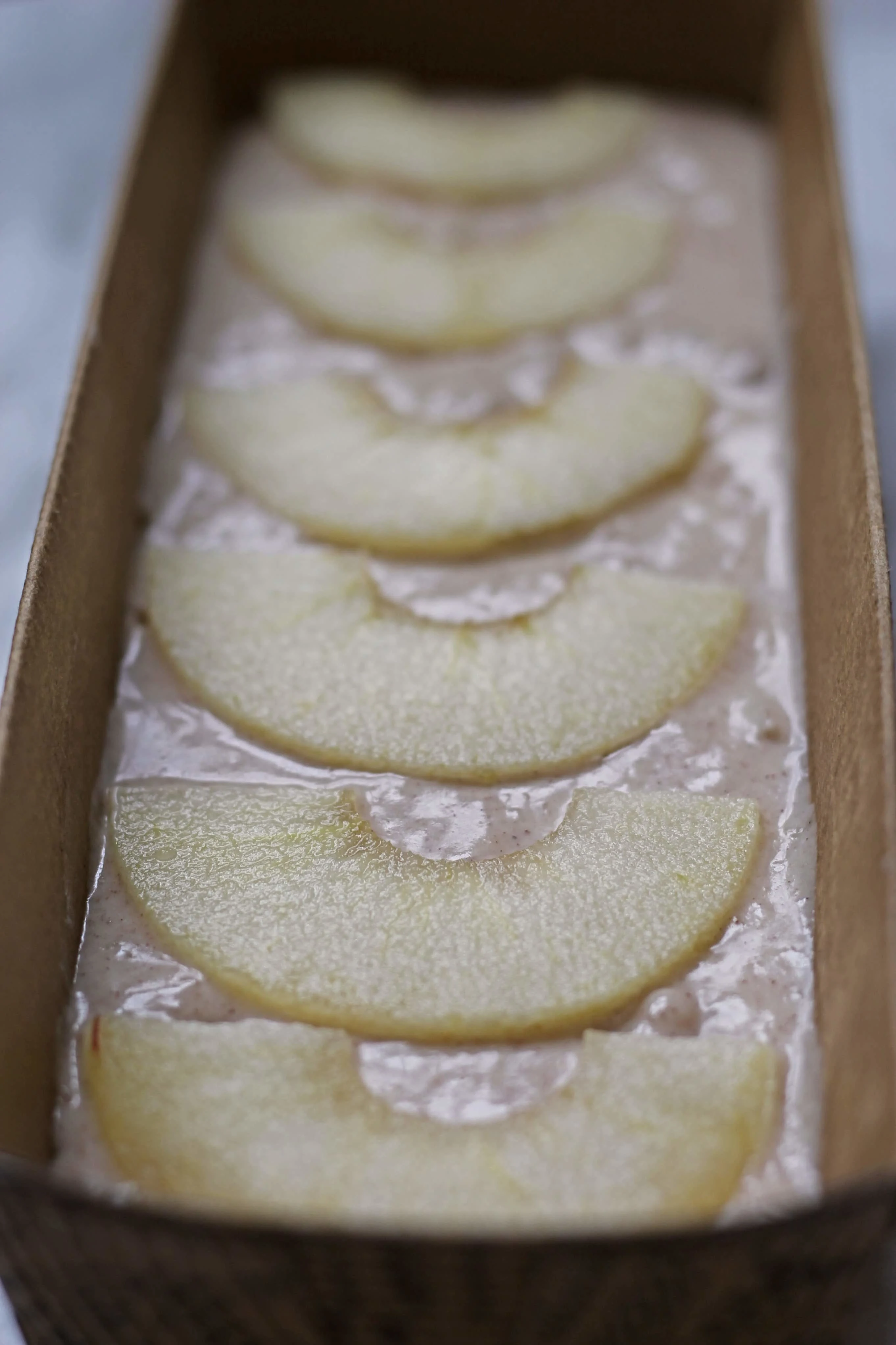 Baking pan with apple cake batter topped with thinly sliced apples.