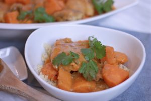 White serving bowl full of Moroccan Chicken Stew with wooden spoon and fresh cilantro