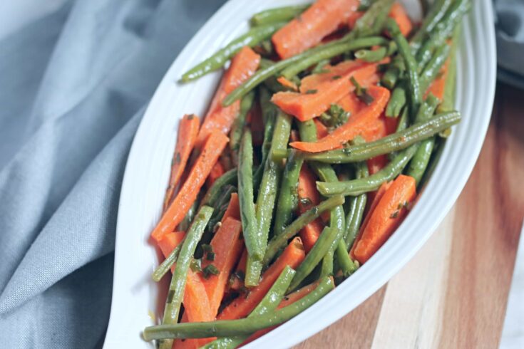 Close up of cooked carrot sticks and green beans in white ceramic serving dish