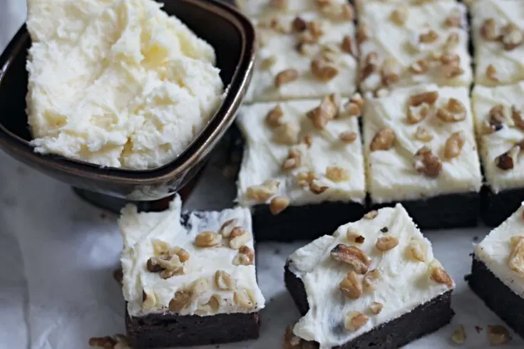 Banana Brownie Squares on parchment paper with bowl of frosting