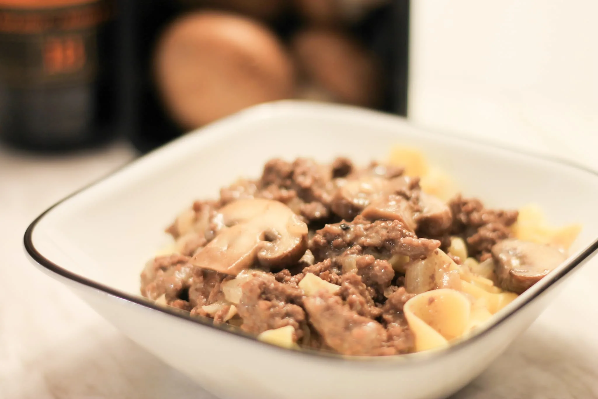 Ground Beef Stroganoff in white dish with cremini mushrooms blurred behind