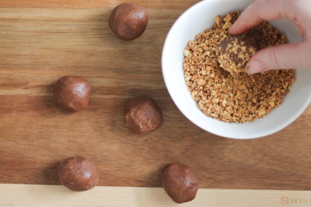 Cutting board with white bowl filled with crushed almonds for rolling chocolate thumbprint cookie balls