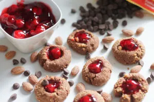 Cherry Chocolate Thumbprint cookies on counter with bowl of cherry filling and spilled chocolate chips