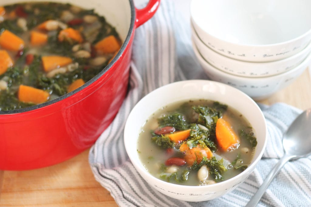 Bowl of kale soup on table with Dutch oven full of soup next to it.