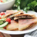 White plate with pita bread tuna melt and fresh cucumber salad