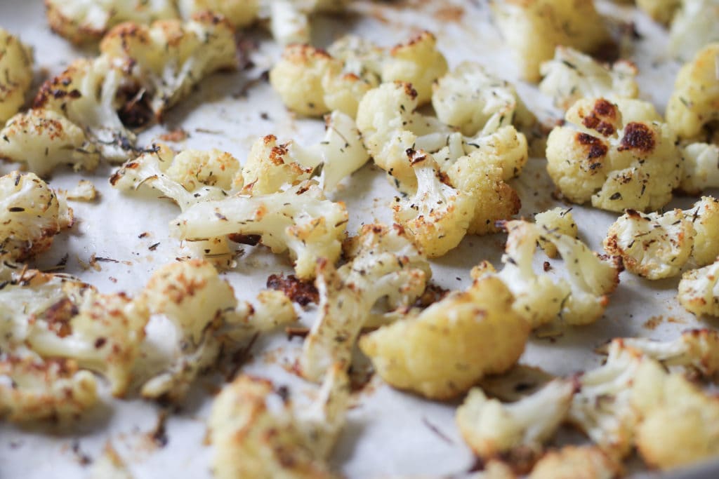 cooked cauliflower with herbs on baking sheet with parchment paper