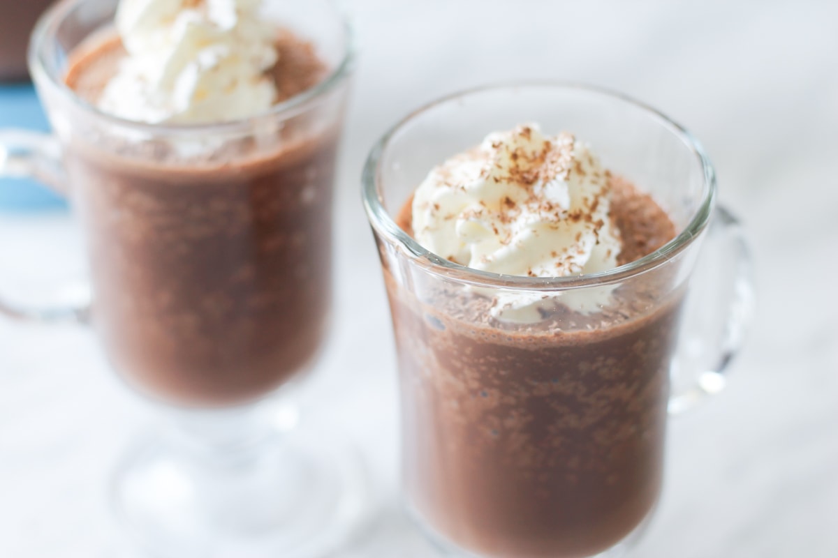 Two clear mugs filled with frozen hot cocoa and topped with whipped cream