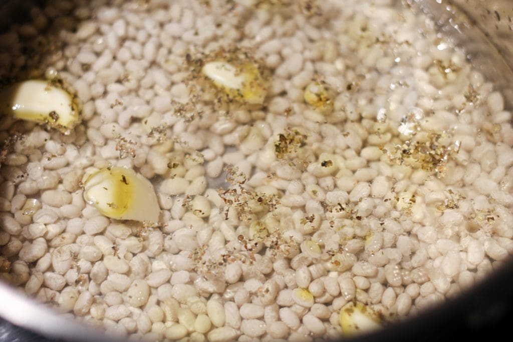 Saucepan with white beans, garlic, spices and olive oil cooking.