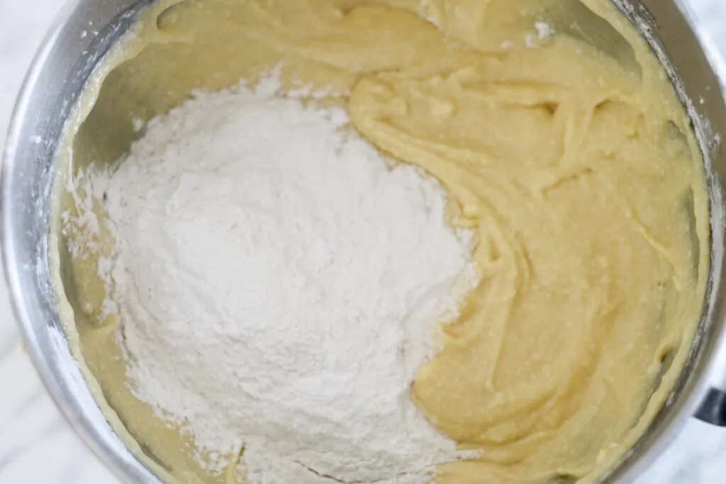 Dry ingredients added to wet lemon cake batter in stainless mixing bowl.