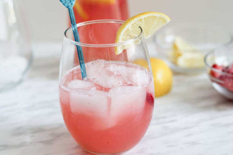 Glass of rhubarb lemonade with stir stick and lemon wedge on counter top.