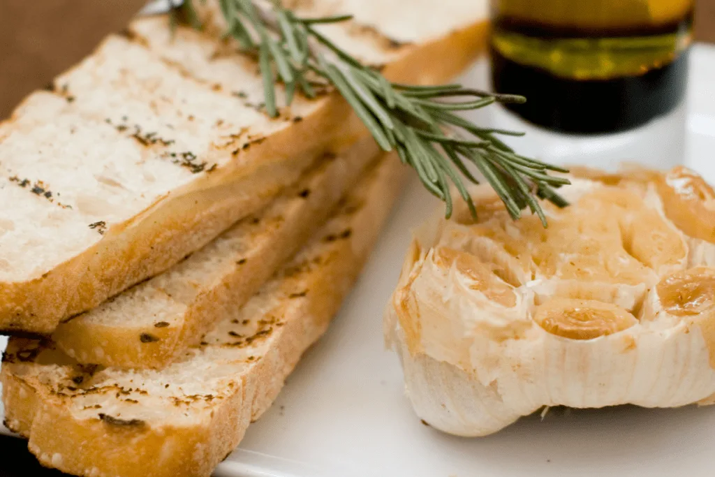 Roasted garlic appetizer on cutting board with fresh bread and rosemary.