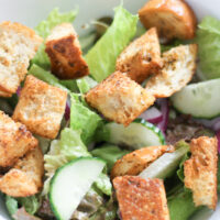 Bowl of green salad topped with croutons.