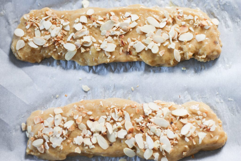 2 logs of biscotti dough with almonds on baking sheet.
