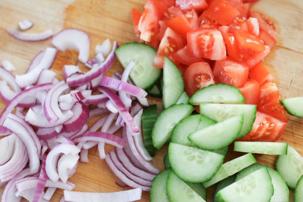 Wooden cutting board with chopped onions, cucumber and tomatoes for salad.
