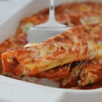Cooked manicotti pasta in baking dish being served with silver lasagna lifter.