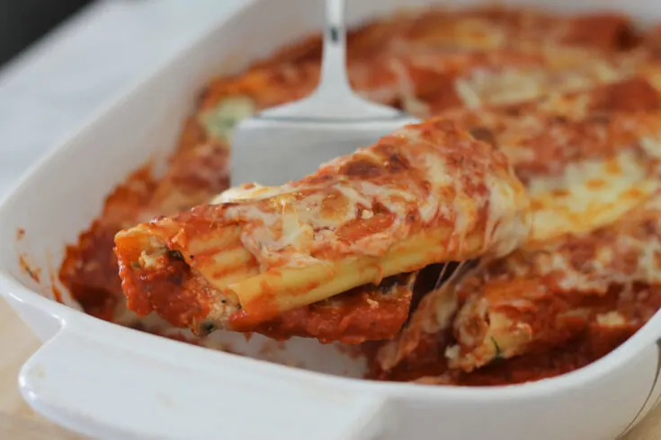 Cooked manicotti pasta in baking dish being served with silver lasagna lifter.