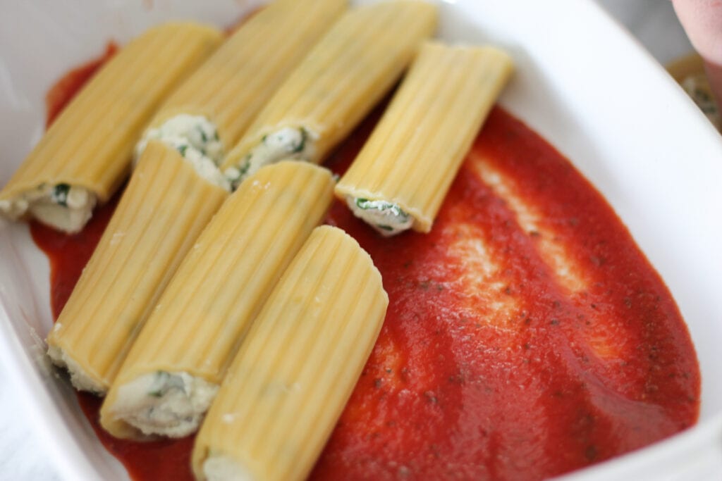 Filled manicotti shells in baking dish with pasta sauce on bottom.
