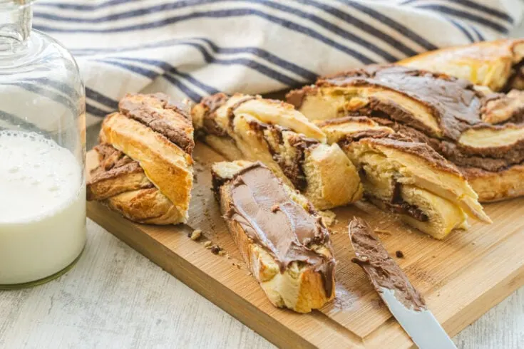 Sliced Nutella Bread on wooden cutting board with a knife resting covered in Nutella.