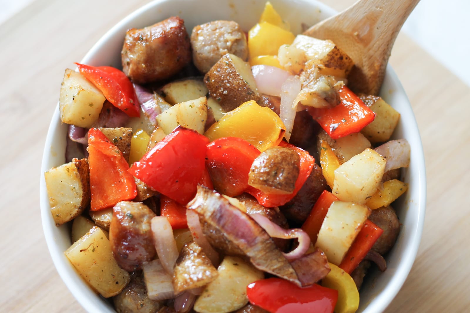 White bowl filled with cooked air fryer sausage, potatoes and mixed bell peppers.