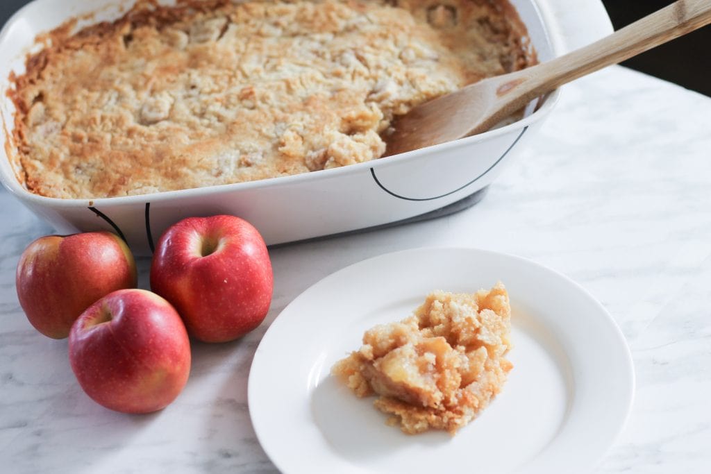 Casserole dish with freshly baked apple dump cake on table with fresh apples.
