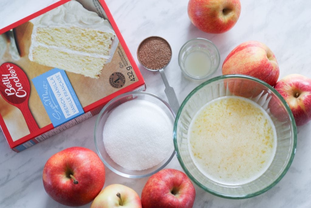 Ingredients for cake arranged on countertop with fresh apples around it. 