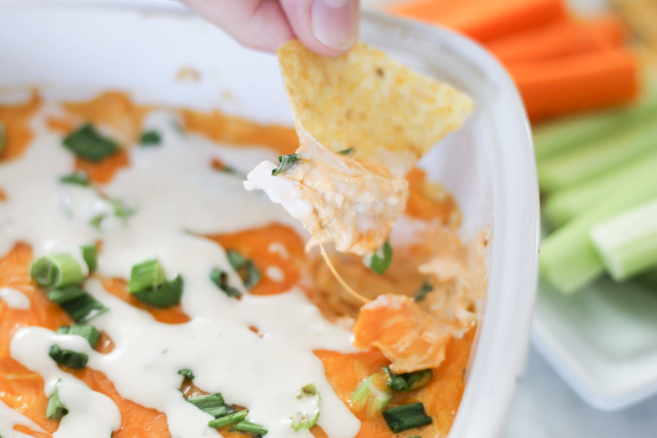 Buffalo chicken dip in white ceramic dish with tortilla chip scooping some out.
