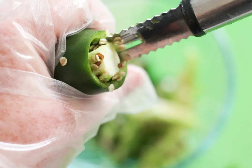 Holding jalapeno while wearing food safe gloves and using a jalapeno coring tool to remove seeds/membrane. 