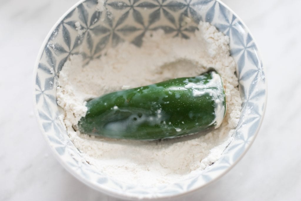 Stuffed jalapeno dipped in milk sitting in flour to be coated. 